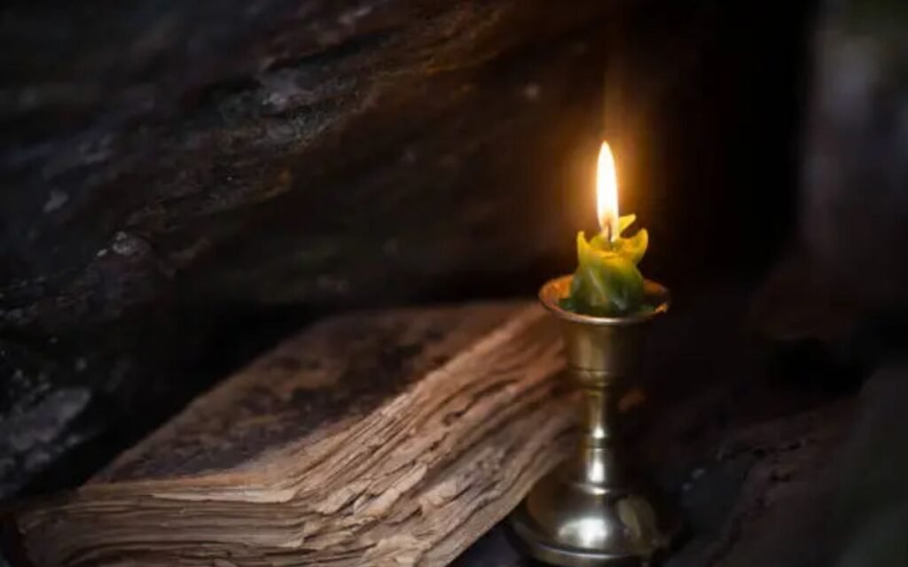 Magic theme. Burning candle and old book in stone dark niche in the forest, close up, selective focus. Foreboding, November, autumn, witchcraft, mystery, victorian style, gothic concept