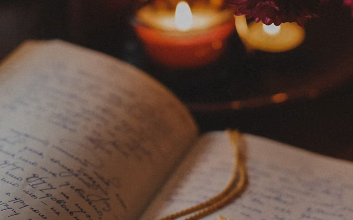 An open book with a tassel on top of it and two small lit candles.